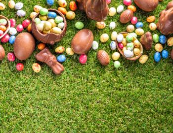 Various candy and chocolate Easter eggs, bunny and rabbits with basket for eggs on green grass park or garden background