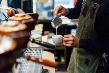 A coffee shop barista pouring milk into a latte