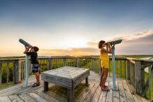 Siblings looking through binoculars at Pea Island national wildlife refugee, North Carolina.