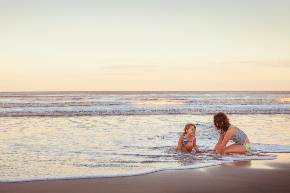 Two children sitting in a shallow beach surf with ocean in background