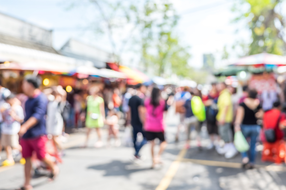 blurry image of people walking through a street fair or market 
